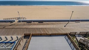 A beach view from a wooden deck with a railing, a lifeguard tower, and a clear sky. - Oceanfront Three Bedroom Condo on the Boardwalk (Ocean City)