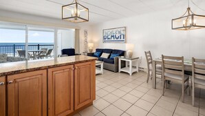 A spacious living area with a kitchen island, a dining table, and a view of the ocean. - Oceanfront Three Bedroom Condo on the Boardwalk (Ocean City)
