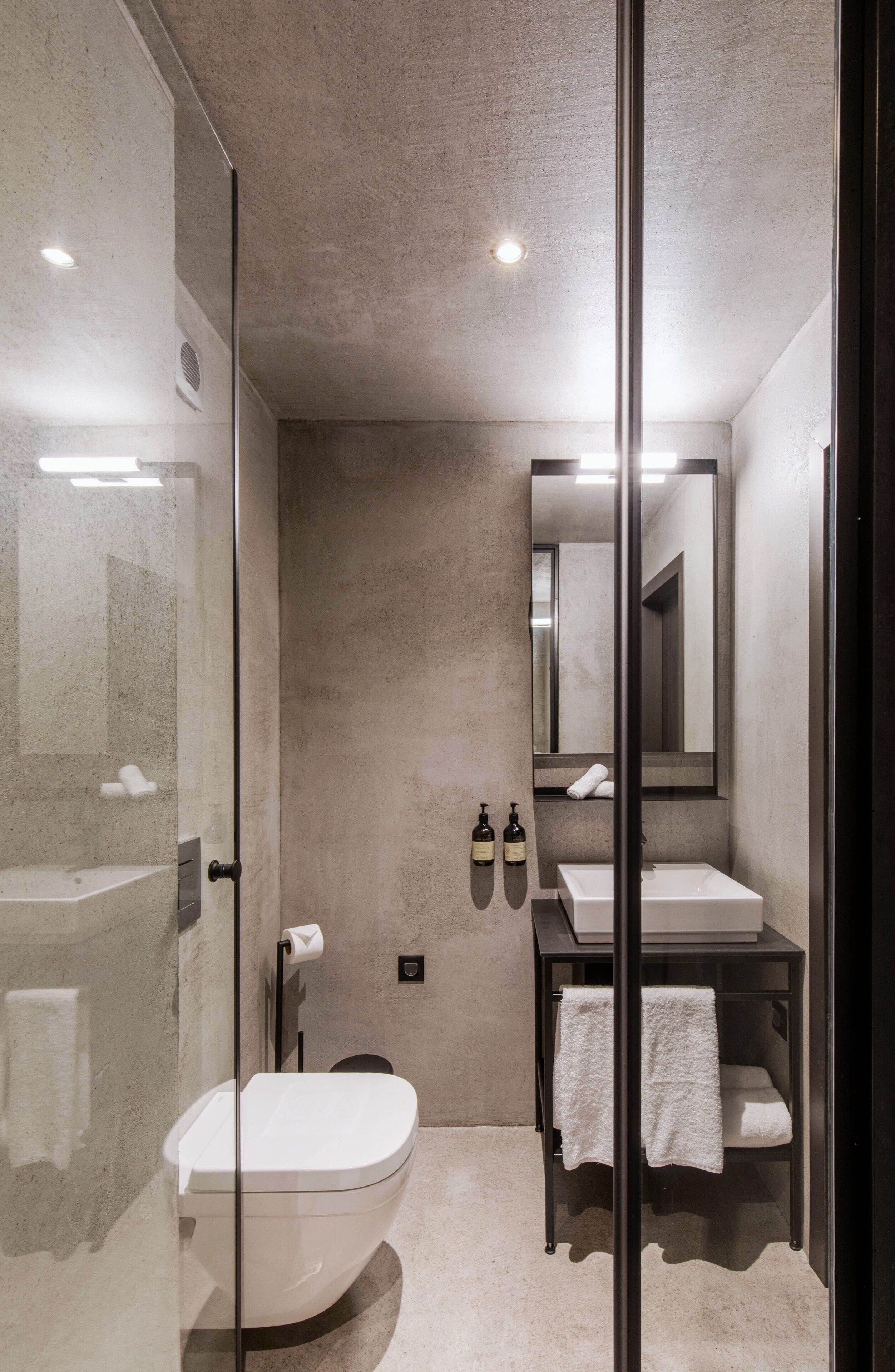 Un baño moderno con cabina de ducha de vidrio, inodoro blanco, lavamanos con espejo y un perchero para toallas.