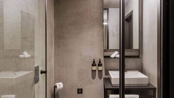Un baño moderno con cabina de ducha de vidrio, inodoro blanco, lavamanos con espejo y un perchero para toallas.