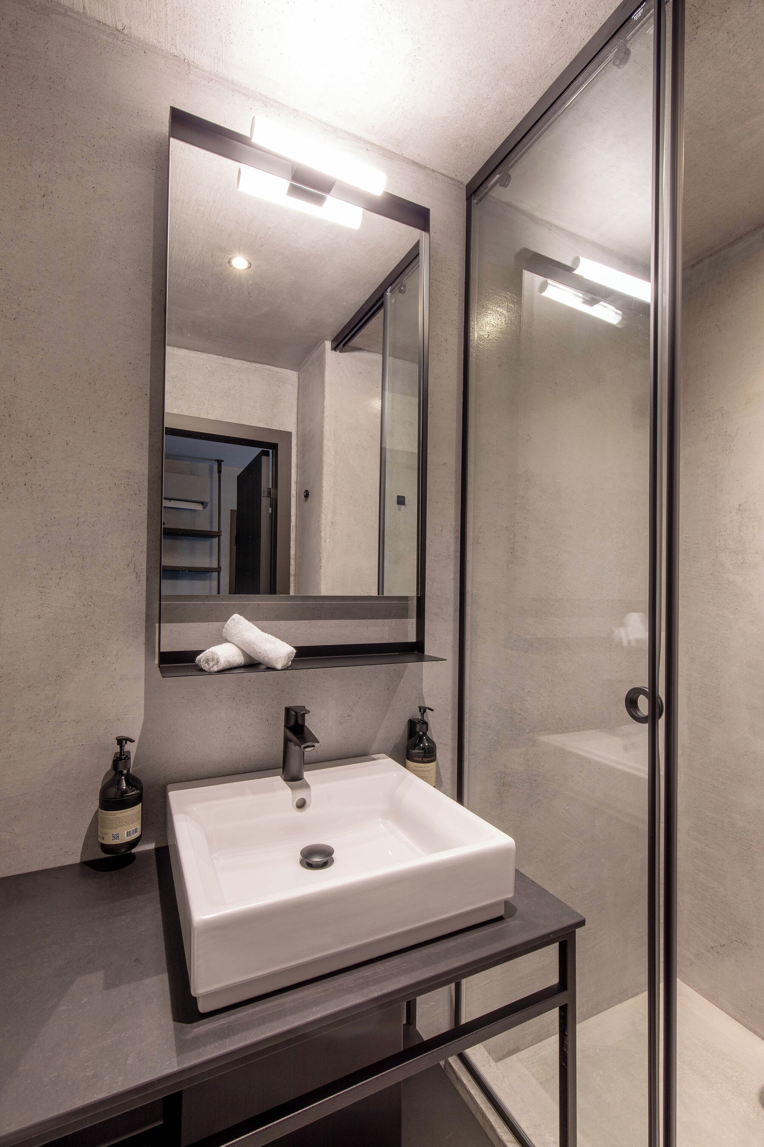 Un baño moderno con lavamanos blanco, un espejo grande y cabina de ducha de vidrio.