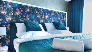 Una cama bien hecha con ropa de cama color turquesa y almohadas blancas, un fondo de papel tapiz floral y una cortina azul oscuro.