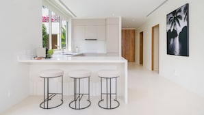 Une cuisine moderne avec des meubles blancs, un îlot central doté de tabourets et une grande fenêtre donnant sur un paysage verdoyant.