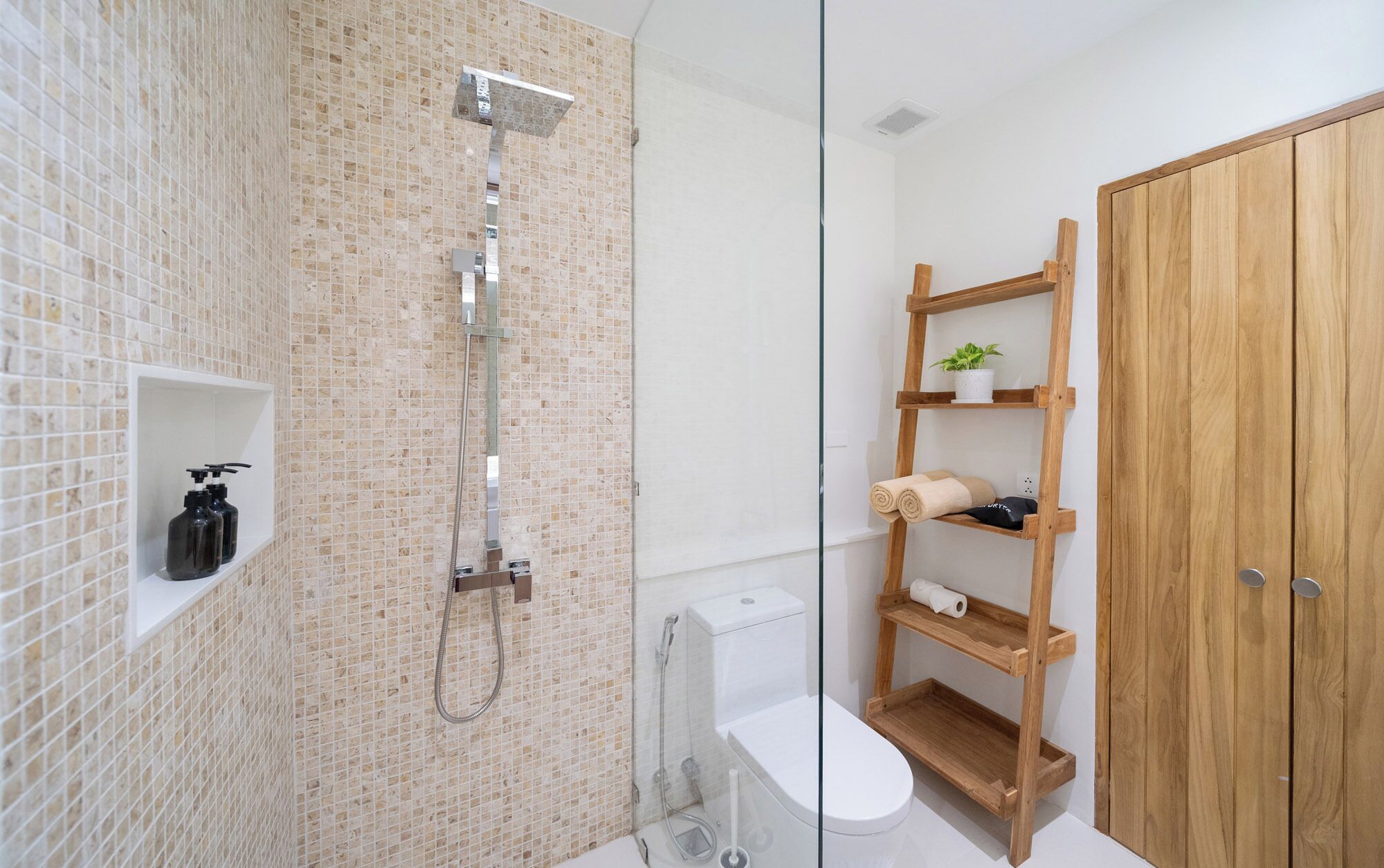 Une salle de bain équipée d’une douche, de toilettes et d’étagères en bois où sont rangés les articles de toilette.