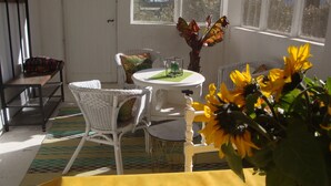 Una habitación iluminada por el sol con sillones de mimbre, una mesa redonda pequeña y un jarrón con girasoles.