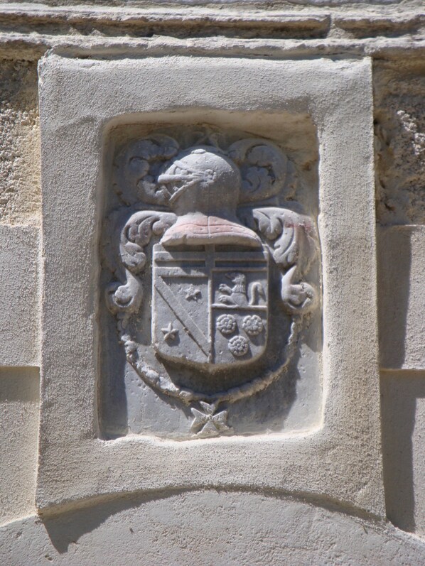 A stone relief of a coat of arms with a shield, helmet, and two supporters.