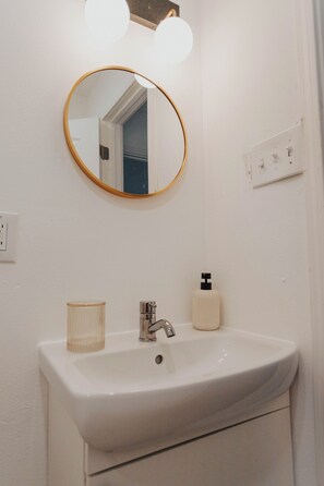 Ein Badezimmer mit einem weißen Waschbecken, einem runden Spiegel mit goldener Rahmung und einer Lampe darüber.