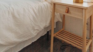 A bedroom with a bed, a bedside table with a lamp, and a window with blinds.