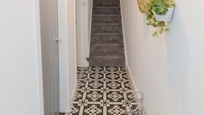 A hallway with a patterned floor, a staircase, and a hanging plant.