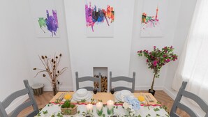 A dining table set for six with white plates, glasses, and cutlery. There are candles, a vase with flowers, and a small plant on the table.