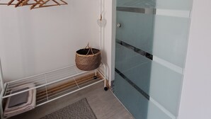 Une pièce avec un mur blanc, un porte-manteau en bois, un panier en osier, un banc en métal et une porte-fenêtre coulissante.