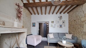 Un salon chaleureux avec un mur en pierre, un canapé gris, un fauteuil blanc, une table basse ronde en bois et un luminaire suspendu.