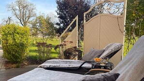 A sunlit outdoor seating area with a cushioned lounge chair, a small table with a drink, and a decorative pot. - Holiday apartment - nature, peace and relaxation (Wangen im Allgäu)