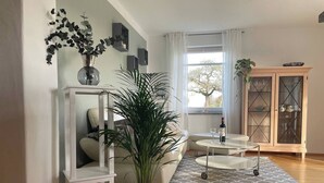 A modern living room with a sofa, a coffee table, a potted plant, and a cabinet with glass doors. - Holiday apartment - nature, peace and relaxation (Wangen im Allgäu)