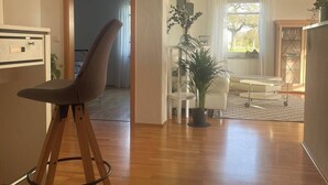 A spacious living area with a wooden floor, a dining table with chairs, a sofa, and a potted plant. - Holiday apartment - nature, peace and relaxation (Wangen im Allgäu)