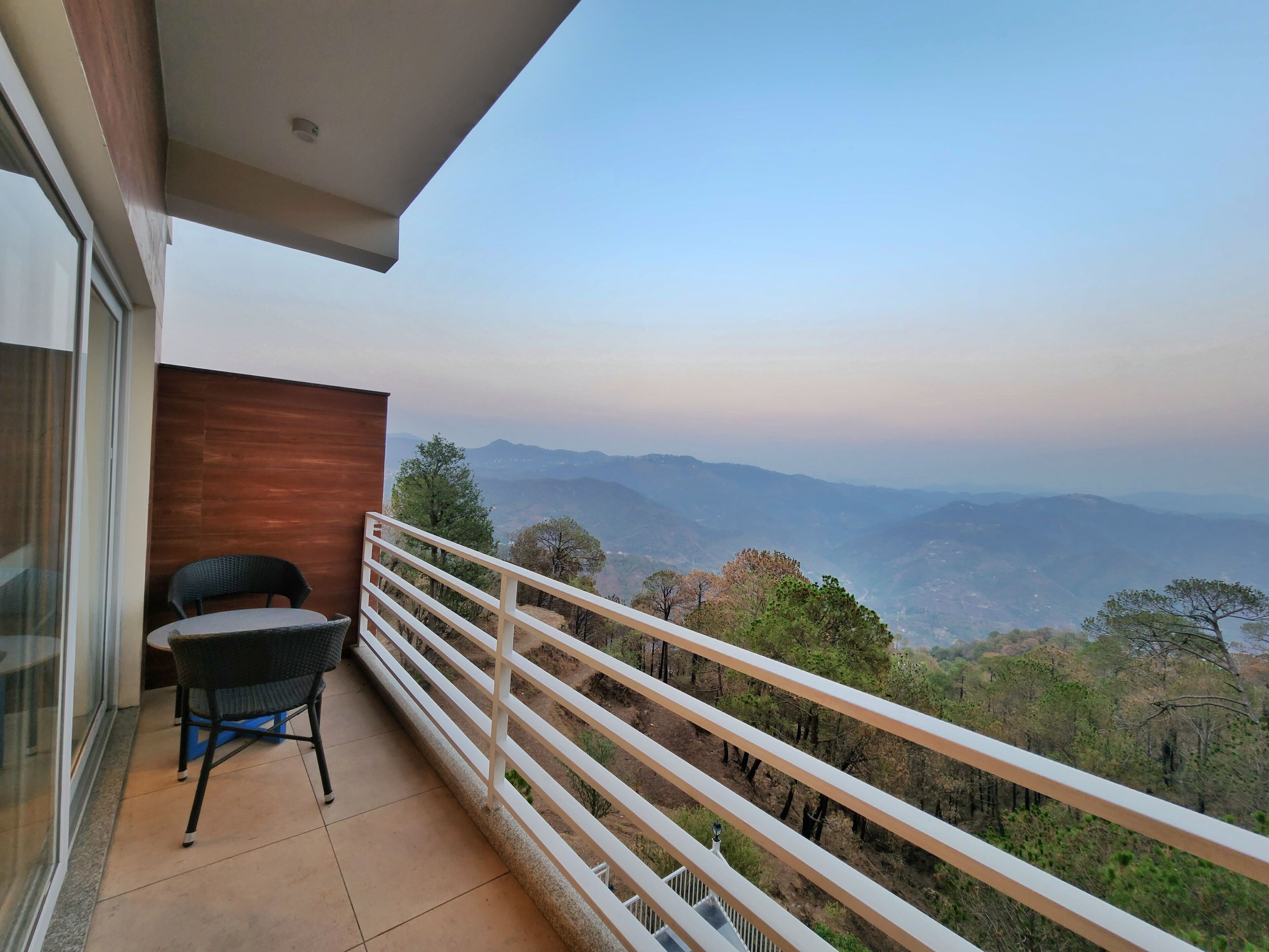 Un balcón con vistas a montañas distantes, una silla y una pequeña mesa.