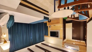 Una habitación de hotel moderna con una cama grande, un televisor de pantalla plana, techo de madera y una cortina azul.