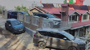 Una zona residencial con varios coches aparcados, un edificio de techo rojo con balcón y una estructura cilíndrica verde en la parte superior.