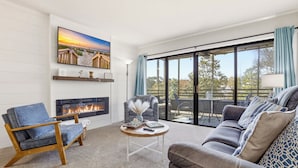 Un salón con chimenea, un sofá, una silla, una mesa de centro y un ventanal con vistas.