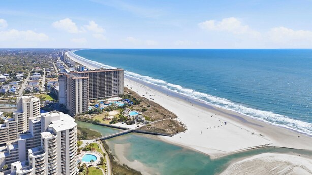 Un hotel costero con varios edificios altos, una playa y un puerto deportivo.