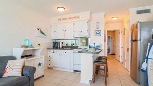 Una cocina compacta con armarios blancos, una cafetera y un letrero que dice 'She sells seashells'.
