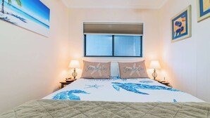 Un dormitorio con una cama, dos mesitas de noche, una ventana con persianas y un cuadro en la pared.