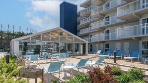 A hotel with a glass-enclosed lounge area, outdoor seating, and a multi-story building with balconies. - Sunset Chaser’s Dream | Bayfront Condo Near the Boardwalk (Ocean City)