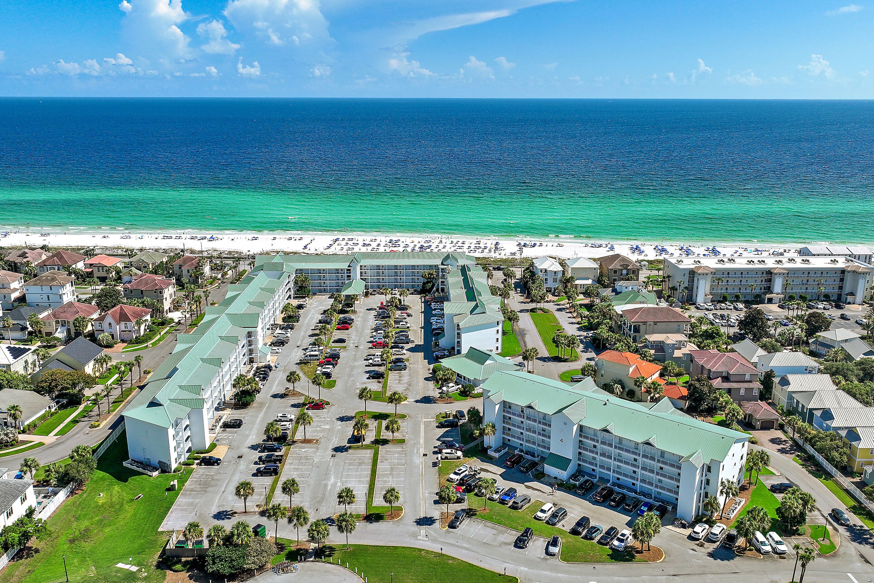 An aerial view of a coastal hotel with multiple buildings, parking lots, and a beach in the background.