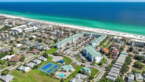 Luftaufnahme einer Küstenwohngegend mit Strand, Schwimmbad und Tennisplatz.