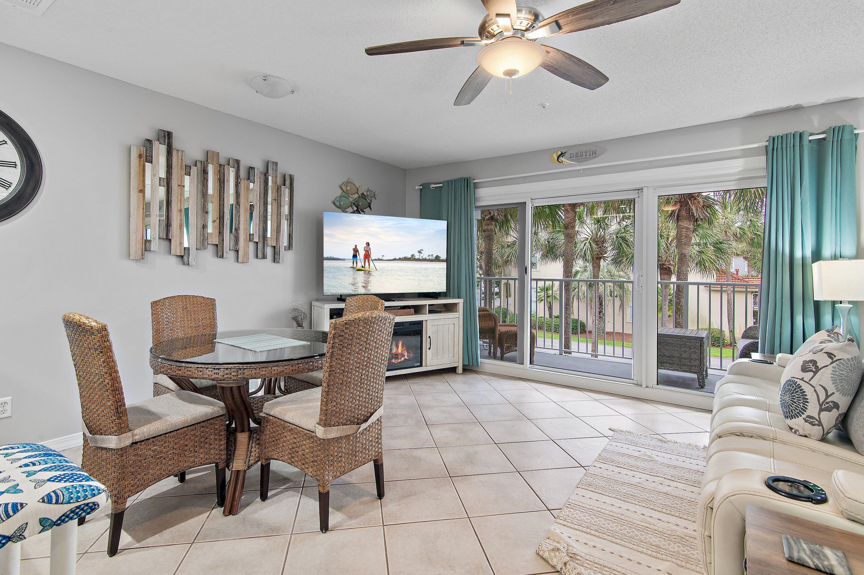 A living room with a TV, wicker chairs, a glass table, a sofa, and a view through large sliding glass doors.