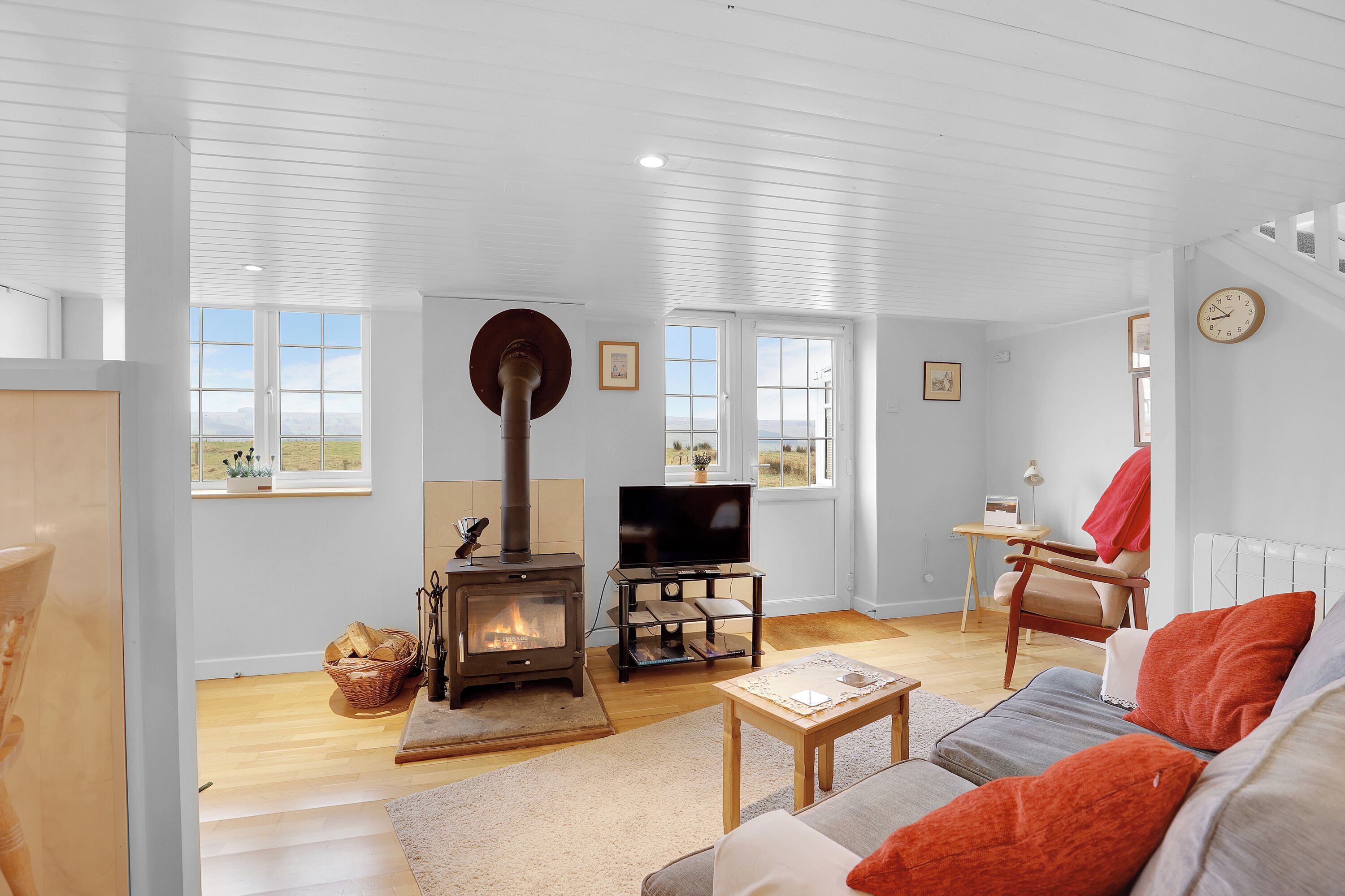 Een moderne woonkamer met een open haard, een televisie en een bank met oranje kussens.