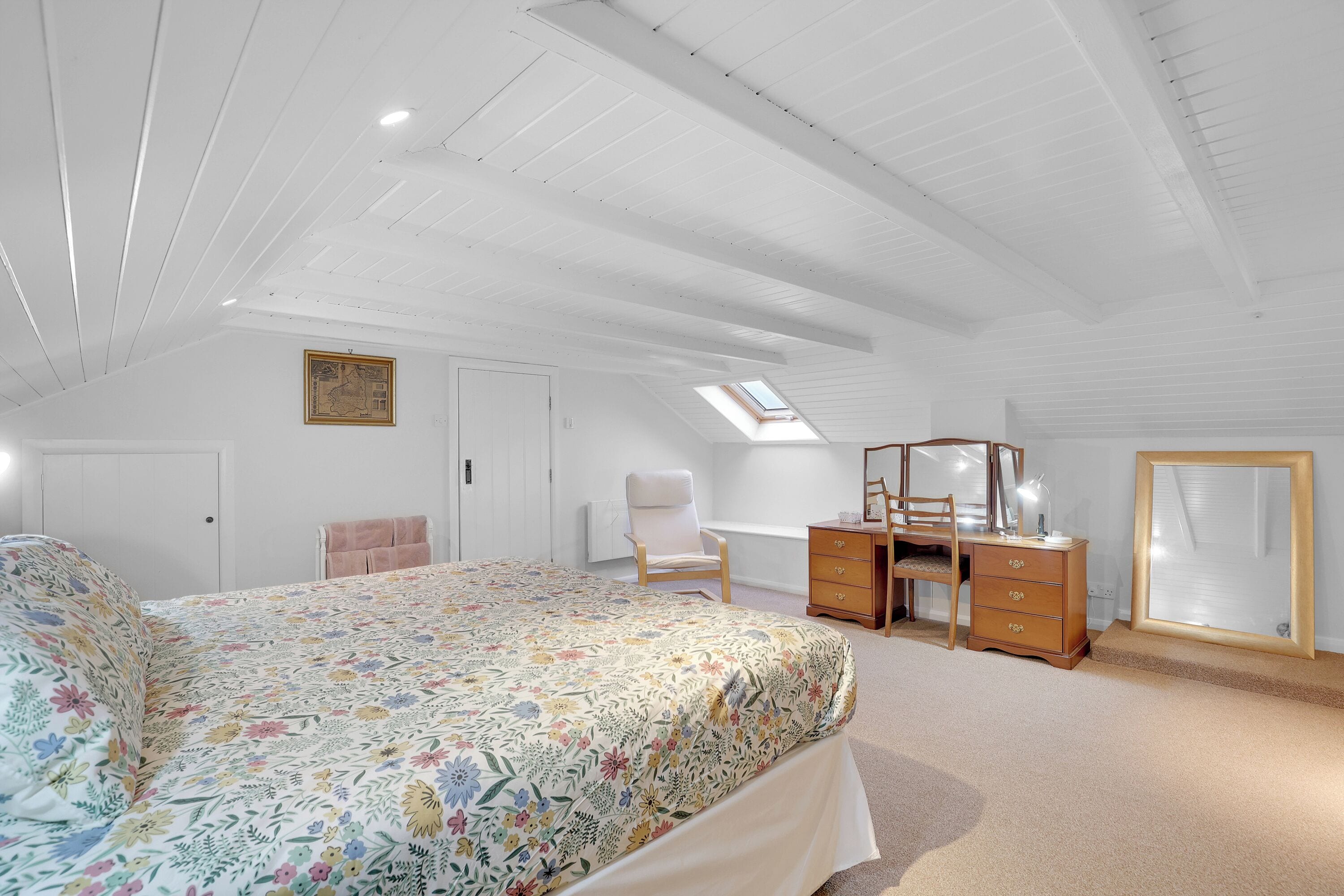 A bedroom with a bed, a desk, a chair, a dresser, a mirror, and a skylight.
