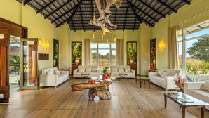 A spacious living room with a high ceiling, wooden flooring, and two white sofas. A unique coffee table made from a tree trunk is in the center. - Sterling Tipeshwar (Kelapur)