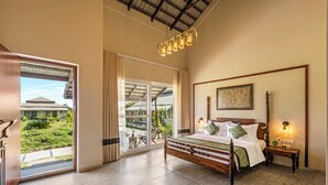 A spacious bedroom with a large bed, a wooden headboard, a nightstand, and a hanging light fixture. - Sterling Tipeshwar (Kelapur)
