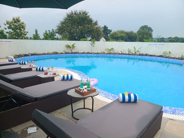 A pool area with lounge chairs, a table with drinks, and a sign indicating a 4-feet depth. - Sterling Tipeshwar (Kelapur)
