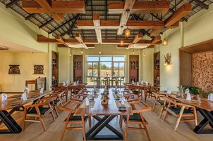 Un comedor con mesas y sillas de madera, ventanas amplias y un techo alto con vigas a la vista.