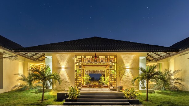 A well-lit entrance with a traditional gate, steps leading up to a covered area, and palm trees on either side. - Sterling Tipeshwar (Kelapur)