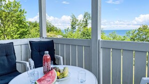 A round table with a watermelon, a bottle of orange juice, and a plate of fruit on a balcony with a view of the ocean. - Nice apartment for 4 guests with WIFI, TV, balcony and pets allowed (Sassnitz)