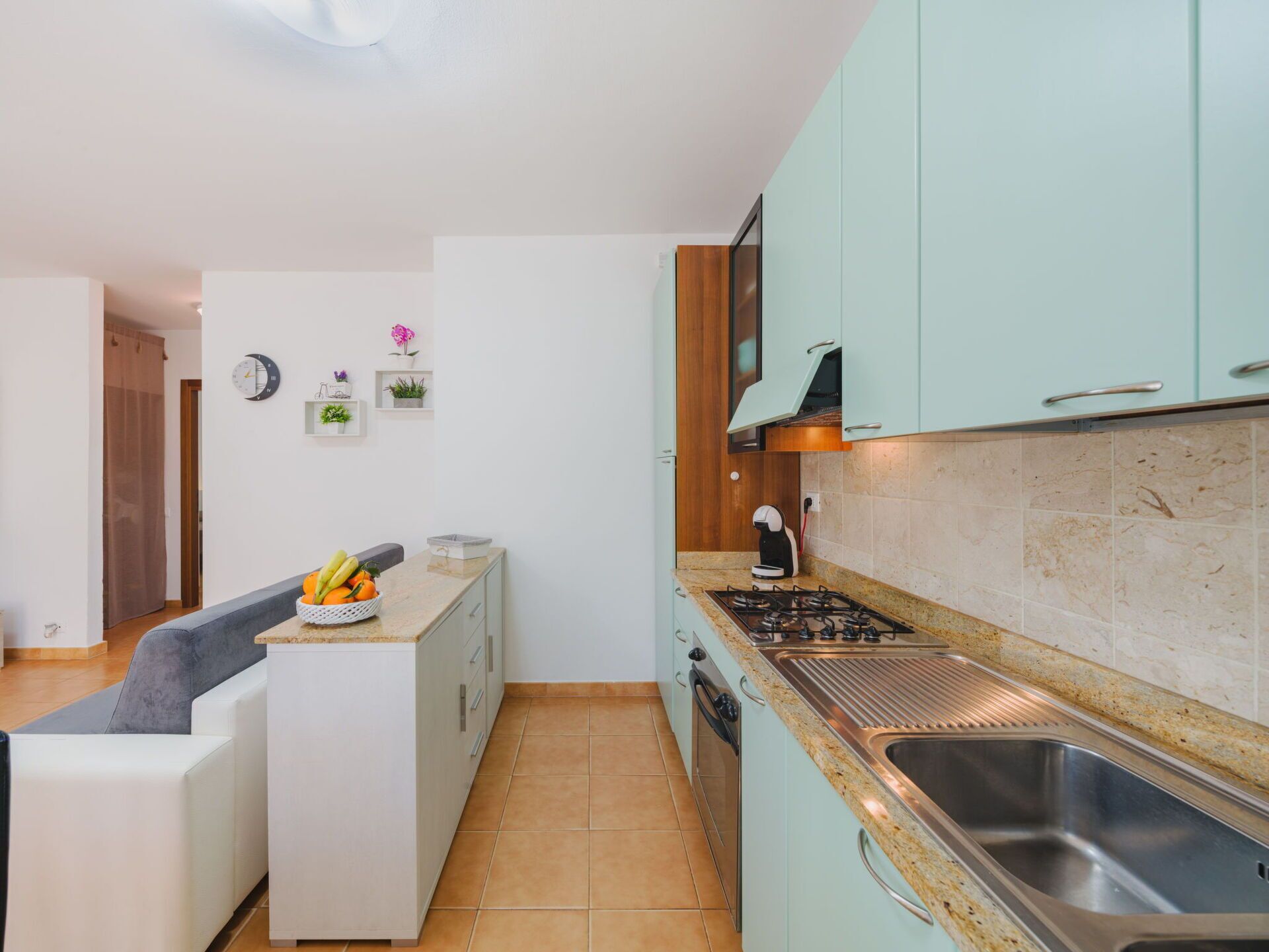 A compact kitchen with teal cabinets, a gas stove, a sink, and a small countertop with a fruit bowl.