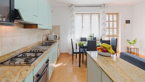 A compact kitchen with a gas stove, microwave, and a dining area with a table and chairs. - Beautiful apartment for 4 people with WIFI, A/C and TV (Massa)