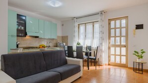 A modern kitchen with teal cabinets, a dining area with a table and chairs, and a grey sofa. - Beautiful apartment for 4 people with WIFI, A/C and TV (Massa)