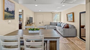 A modern living room with a grey sectional sofa, a wooden dining table with chairs, and a large painting on the wall. - Elegant Green Valley Villa 55+ (Green Valley)