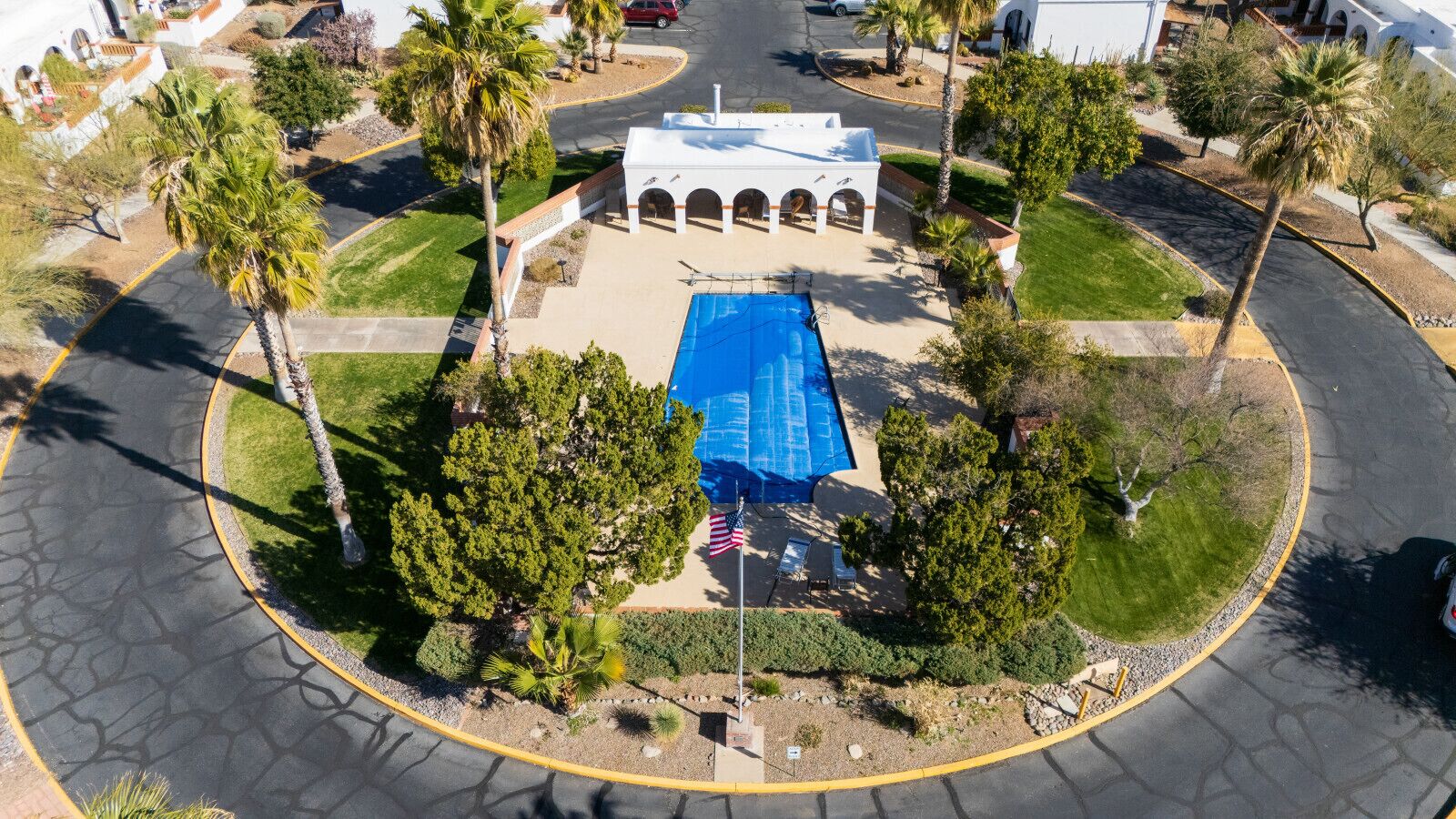 Vue aérienne d’une propriété dotée d’une piscine, de palmiers et d’un bâtiment blanc orné d’arcades.