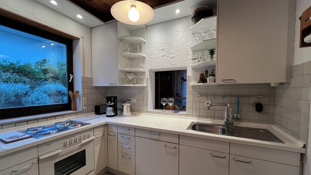 A modern kitchen with white cabinets, a built-in oven, a sink, and a window overlooking greenery.