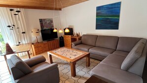 A modern living room with a wooden ceiling, a large sofa, a coffee table, and a painting on the wall.
