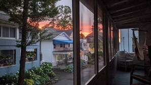 A view from a porch with a wooden railing, overlooking a residential street during sunset. - 28 Morris - Classic, centrally located cottage in Chautauqua Institution! (Chautauqua)