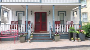 A two-story building with a red door, white and blue trim, and a porch with steps. There are potted plants and a red bench on the porch. - 28 Morris - Classic, centrally located cottage in Chautauqua Institution! (Chautauqua)