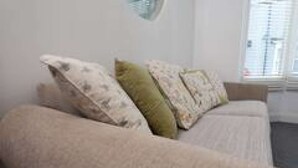 A beige sofa with patterned cushions in a room with a plain wall and a window. - Hampton House Spacious Accommodation In Stockton (Stockton-on-tees)
