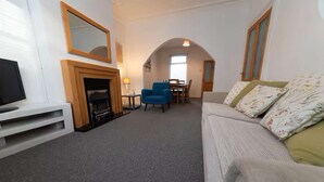A living room with a fireplace, a television, a sofa with patterned cushions, and a dining area with chairs and a table. - Hampton House Spacious Accommodation In Stockton (Stockton-on-tees)