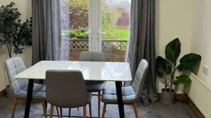 A dining area with a table and chairs, a view of a garden through a glass door, and a potted plant.